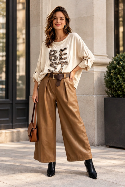 Female model wearing camel belted vegan leather gaucho pants with a cream shirt and black ankle boots